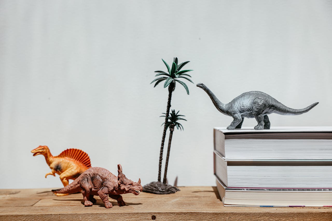 Colorful dinosaur toys and books on a wooden shelf, depicting a playful and educational setup.